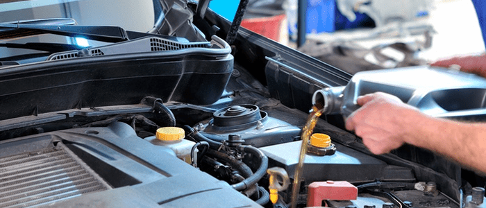 A car engine with a mechanic pouring oil into the oil reservoir as part of basic car maintenance.