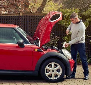 A man stands next to a red car with the bonnet open, he is checking the oil levels to ensure his vehicle is roadworthy.