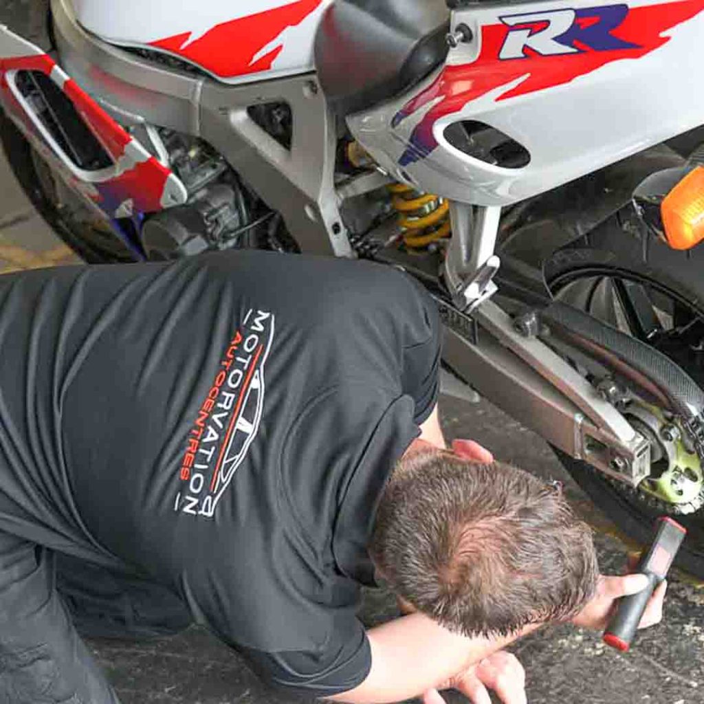 A Motorvation Northampton technician kneeling next to a motorcycle they are conducting an MOT on.