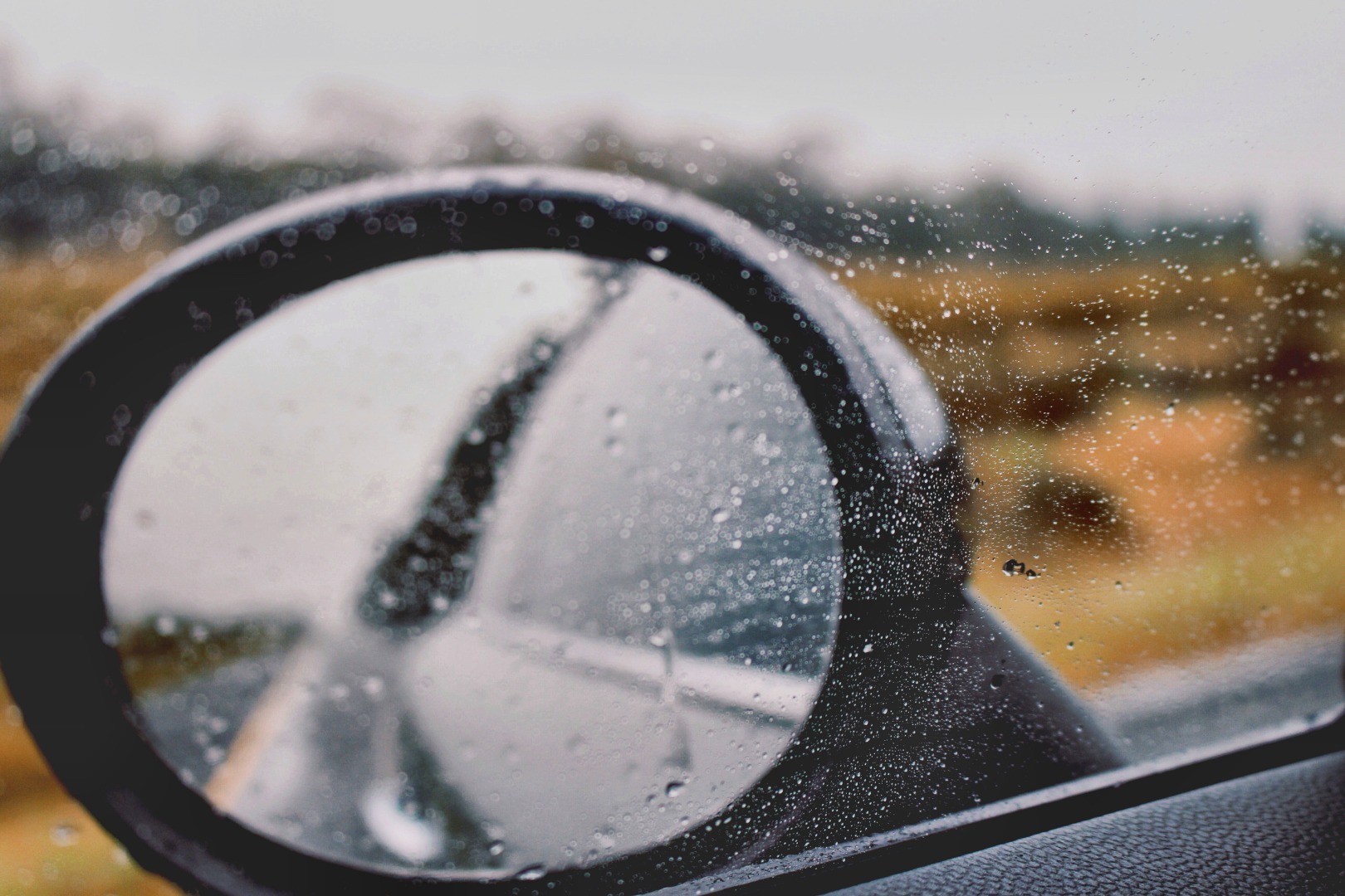 View of car side mirror through the window in the rain